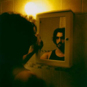 A self portrait shot by Hamza, the image shows a reflection of himself warmly lit, shot on a polaroid camera.